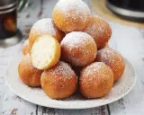Puszyste pączki z piekarnika, posypane cukrem pudrem, kuszą swoim wyglądem. Jeden przekrojony ukazuje idealnie wyrośnięte wnętrze.
