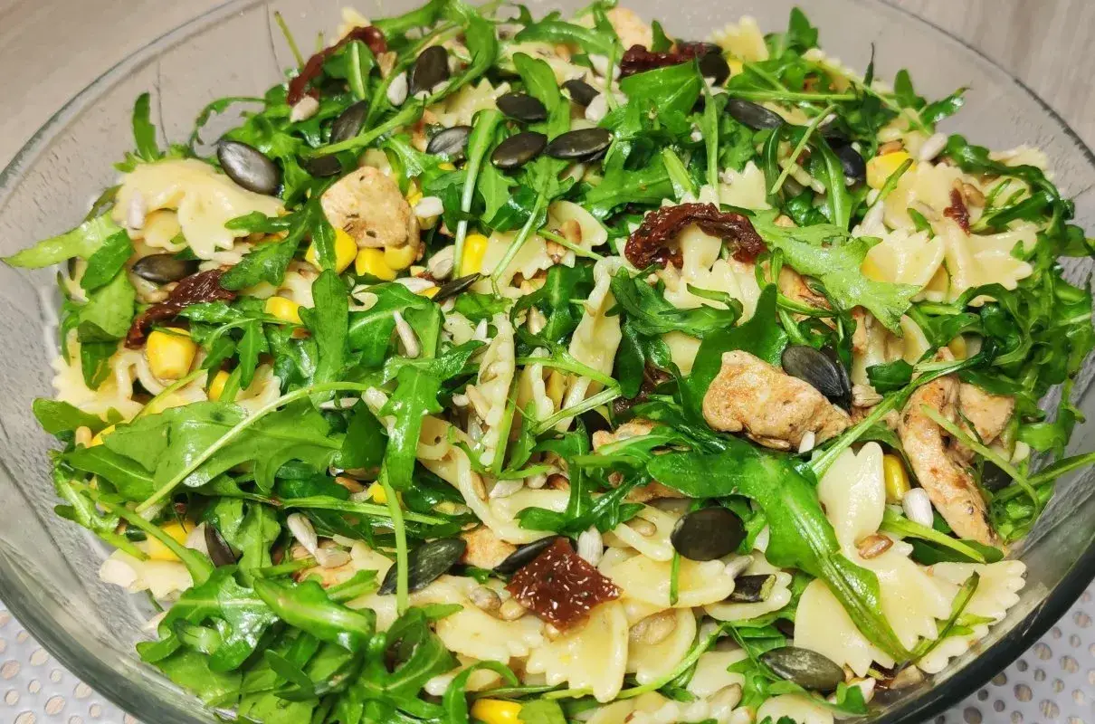 Kolorowa sałatka z makaronem farfalle, rukolą, kurczakiem, kukurydzą i słonecznikiem, wzbogacona o intensywny smak suszonych pomidorów.