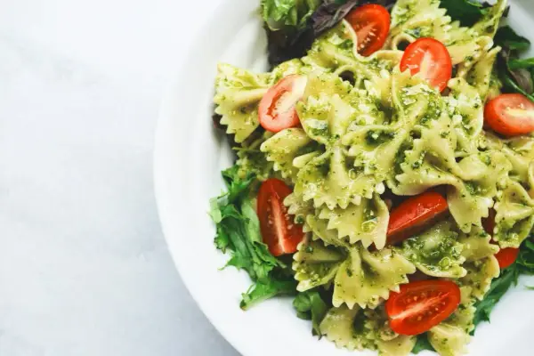 Pyszny makaron z pesto, udekorowany pomidorkami koktajlowymi i świeżą sałatą, podany na białym talerzu.