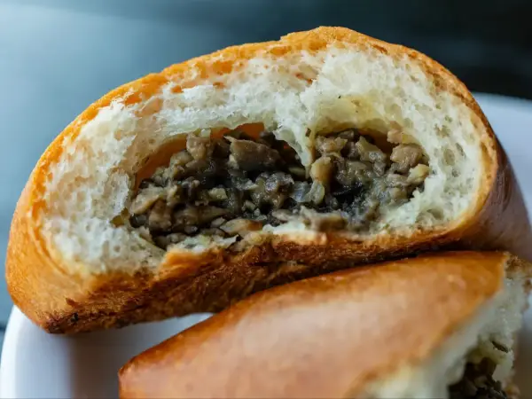 Puszysta bułka z pieczarkami, przekrojona na pół, odsłaniająca aromatyczne, drobno posiekane grzyby.